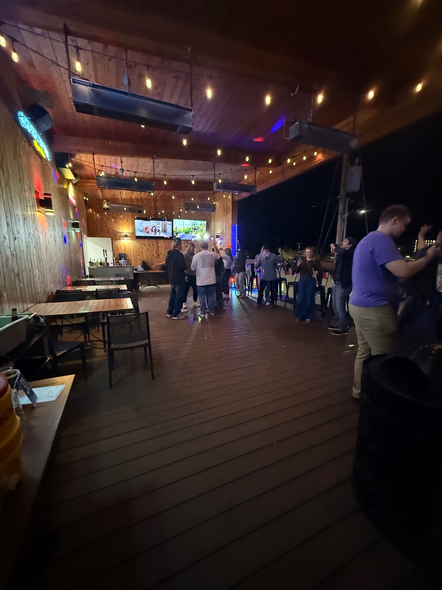 The upstairs deck at night — string lights on and the floor filling up